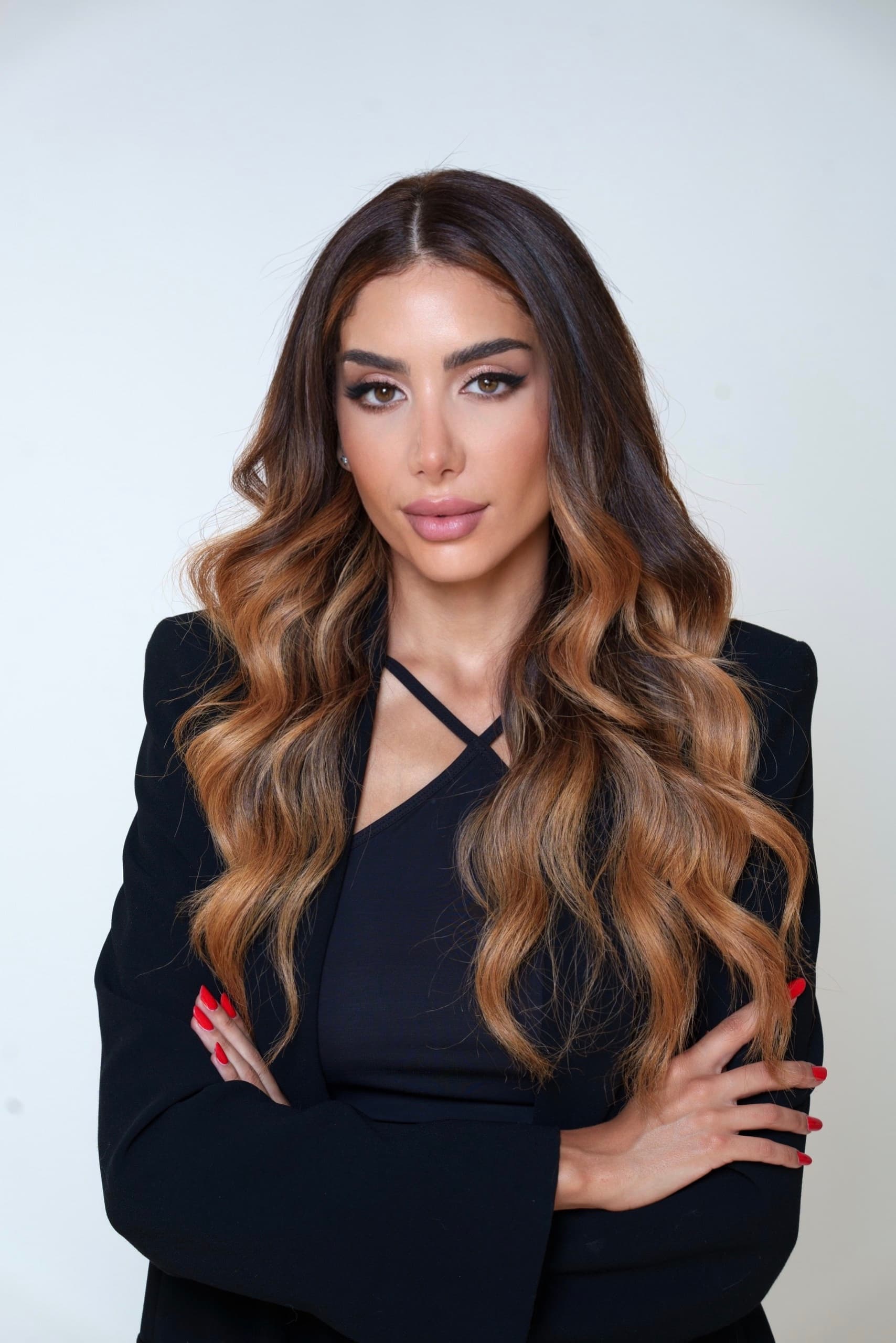 Amira Bechini en studio, en blazer noir, les bras croisés, sur un fond clair.